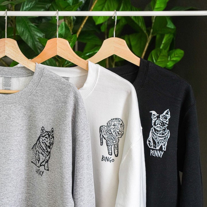gray, white, and black sweatshirts printed with images of dogs hanging on a clothing rack