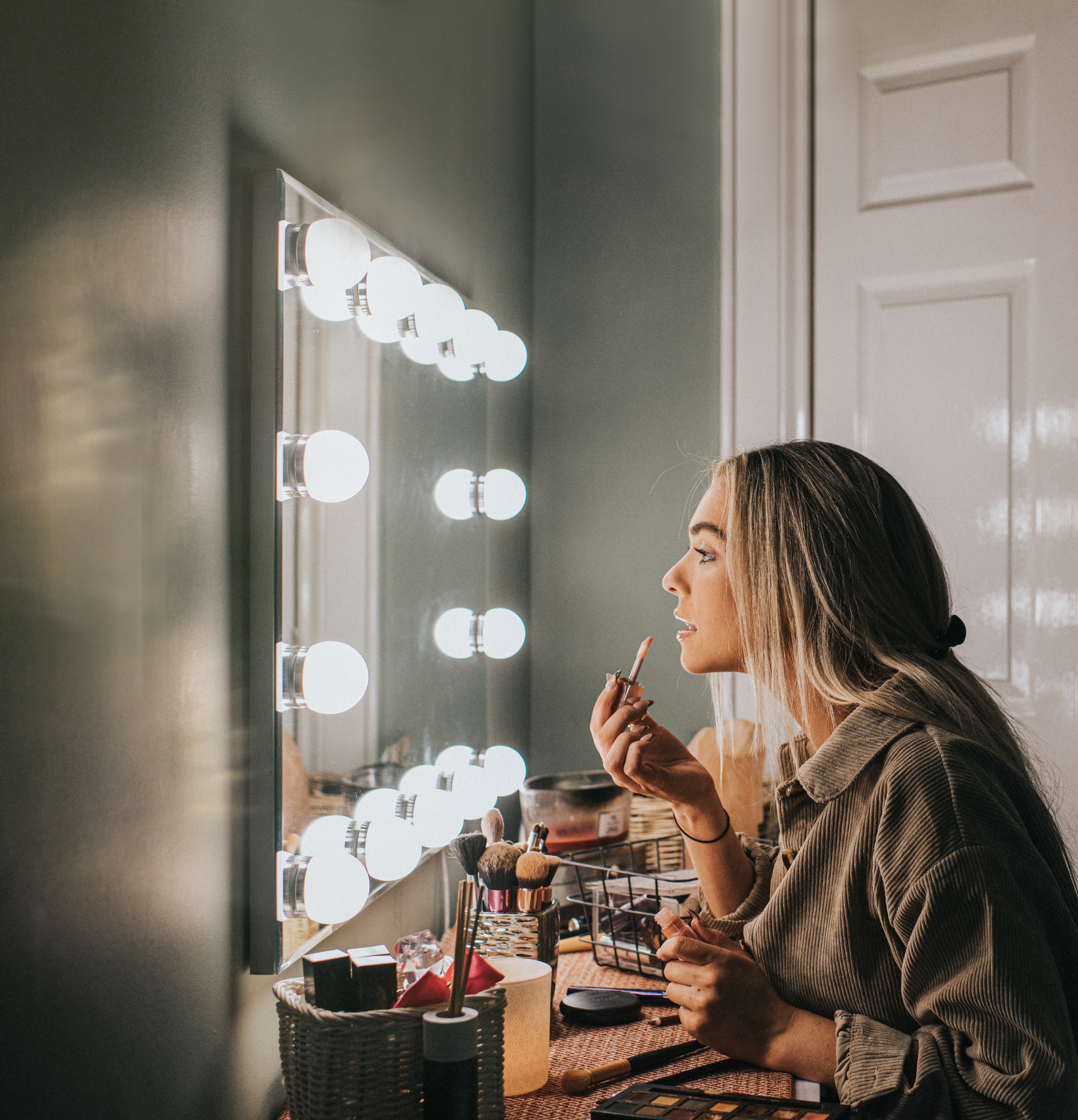 Person applying makeup at a mirror with lights