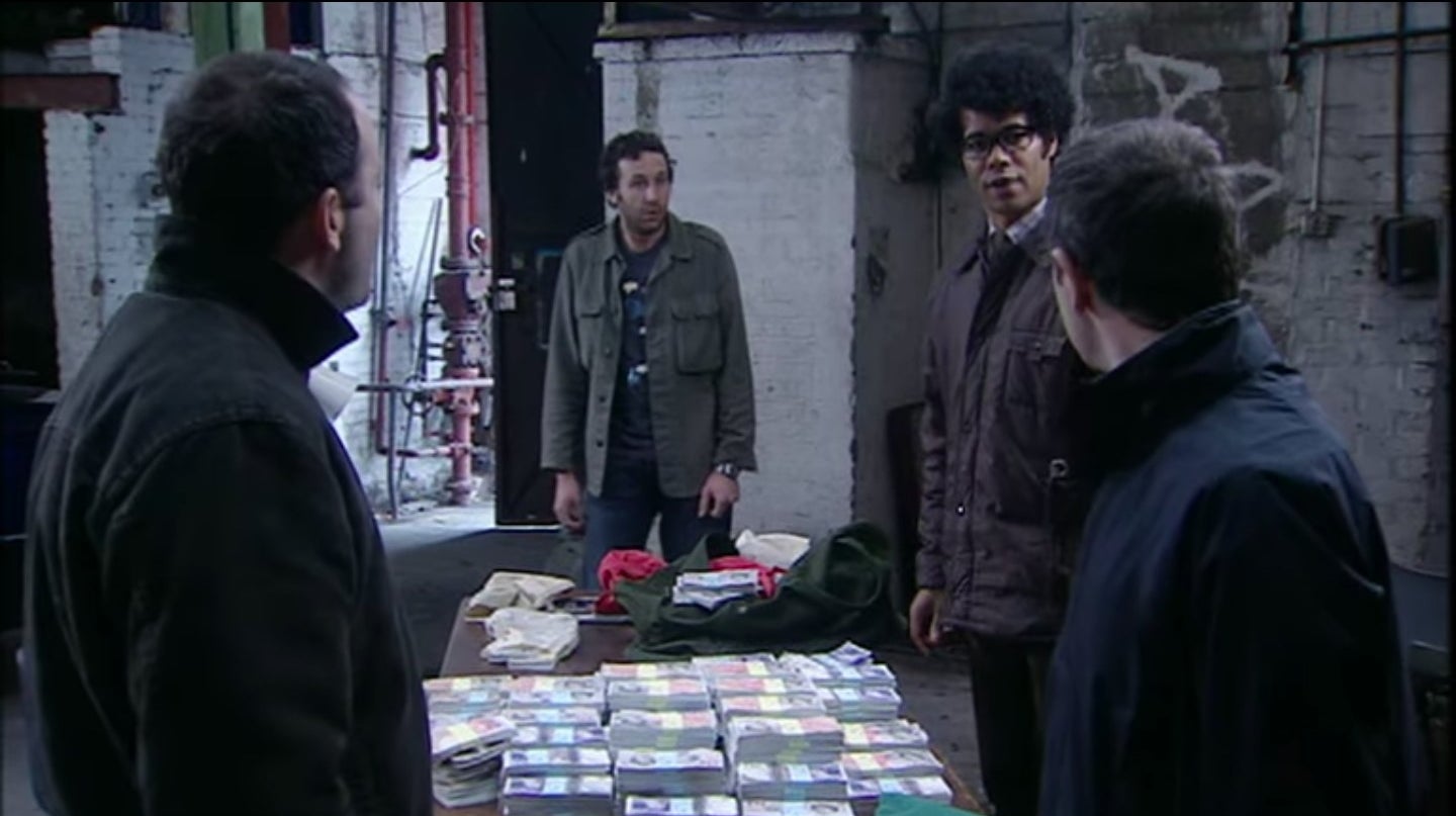 Moss talking to two bank robbers with Roy and a table full of money next to him in &quot;The IT Crowd&quot;