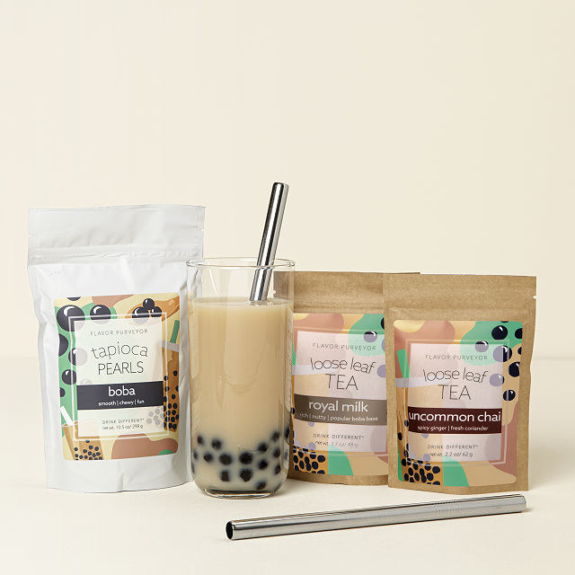 a glass of bubble tea, a straw, and three pouches used to make the drink