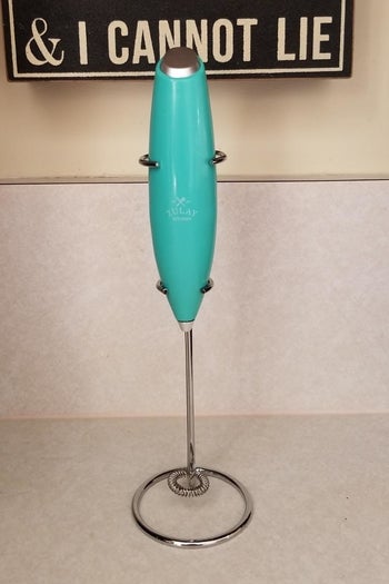 a reviewer photo of the mil frother on the included stand sitting on a kitchen countertopn
