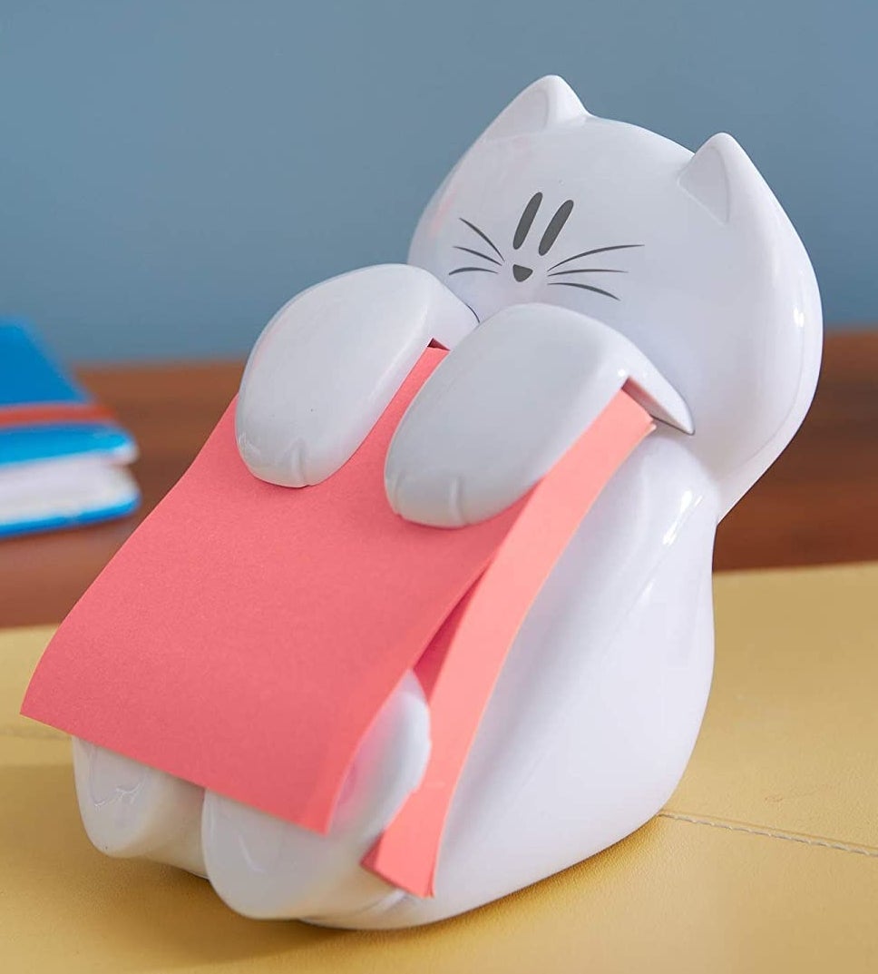 A ceramic cat holding up a block of post-it notes