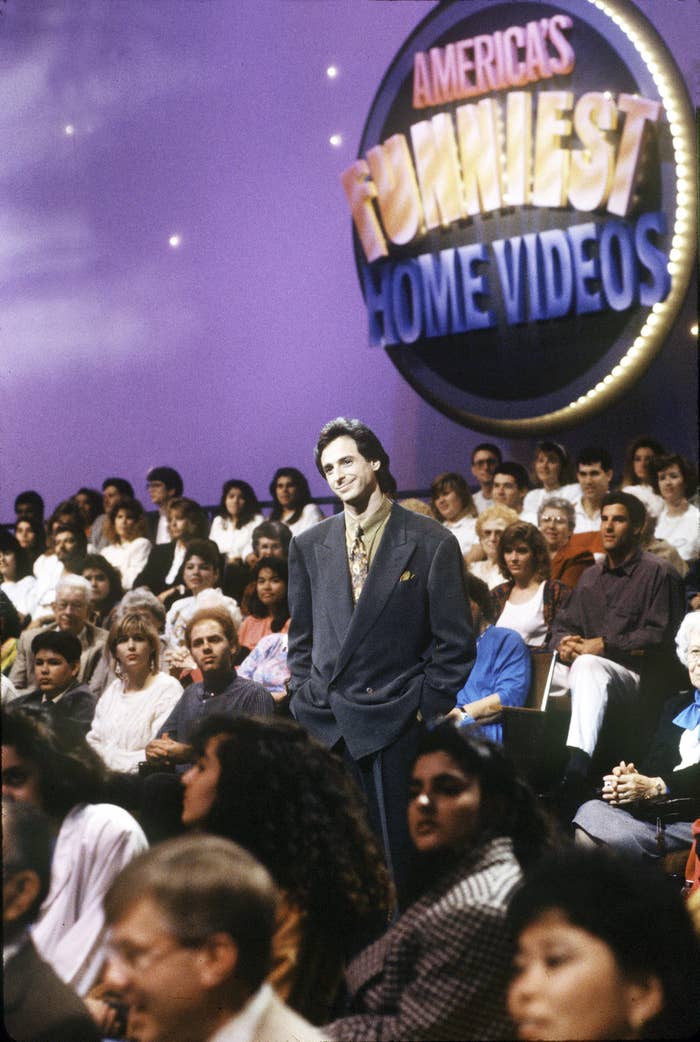 Bob stands in the middle of an audience in front of the show&#x27;s logo