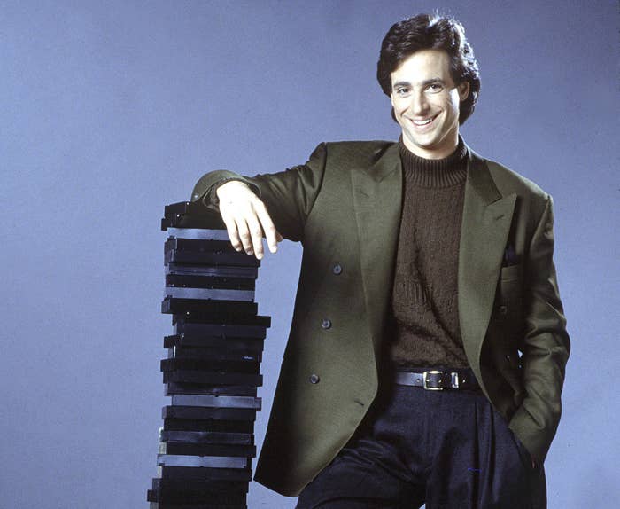 Bob smiles and leans on a large stack of VHS tapes