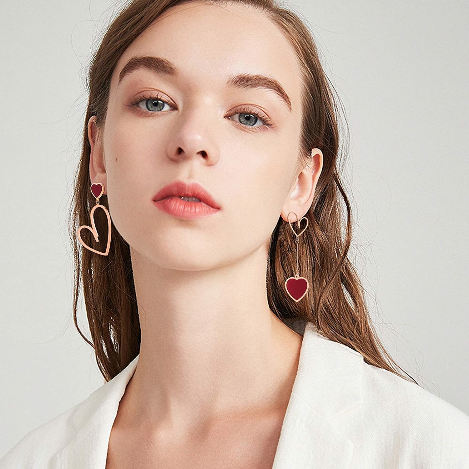 model in gold and red heart earrings, one with a heart charm in drop style and a red heart post and the other with a longer dangle, two medium-size hearts connected by a chain
