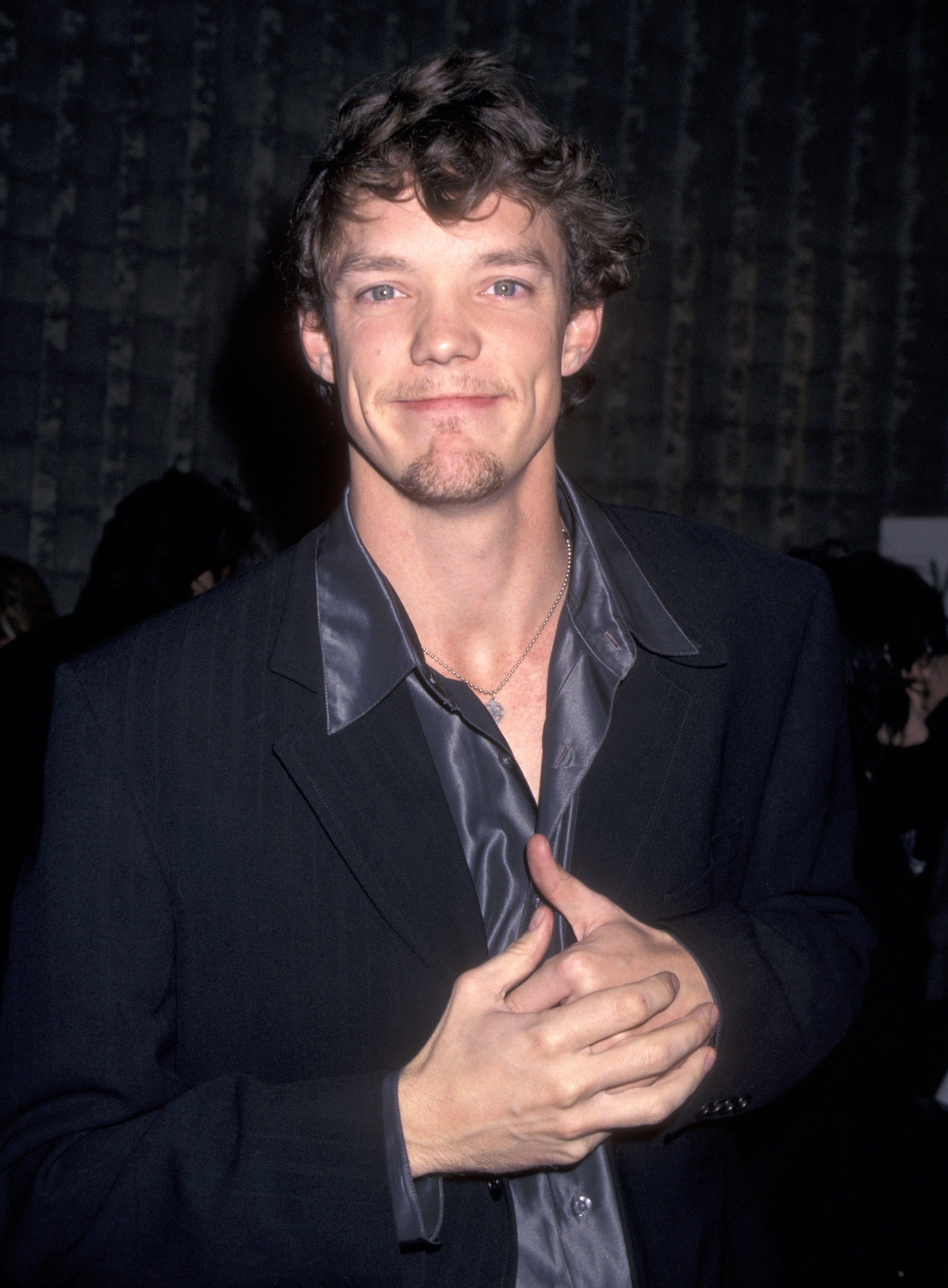 Matthew Lillard in a black suit and a gray shirt with a large collar