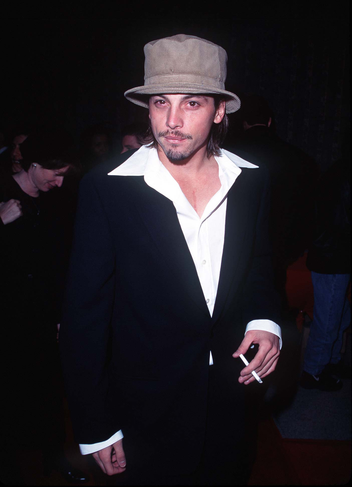 Skeet Ulrich in a bucket hat and black suit and white shirt with a giant collar
