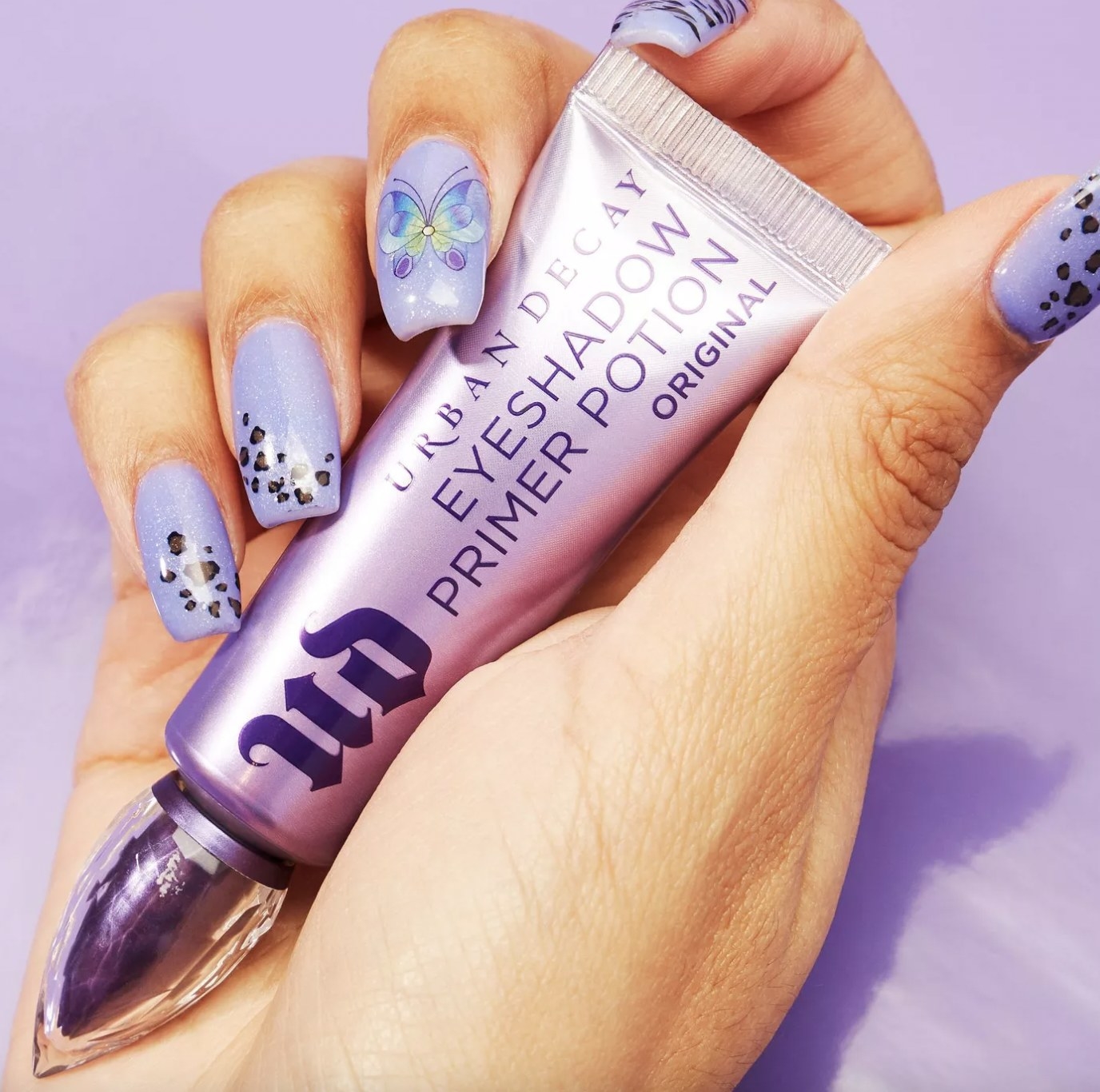 A person with a purple manicure holding a tube of eyeshadow primer