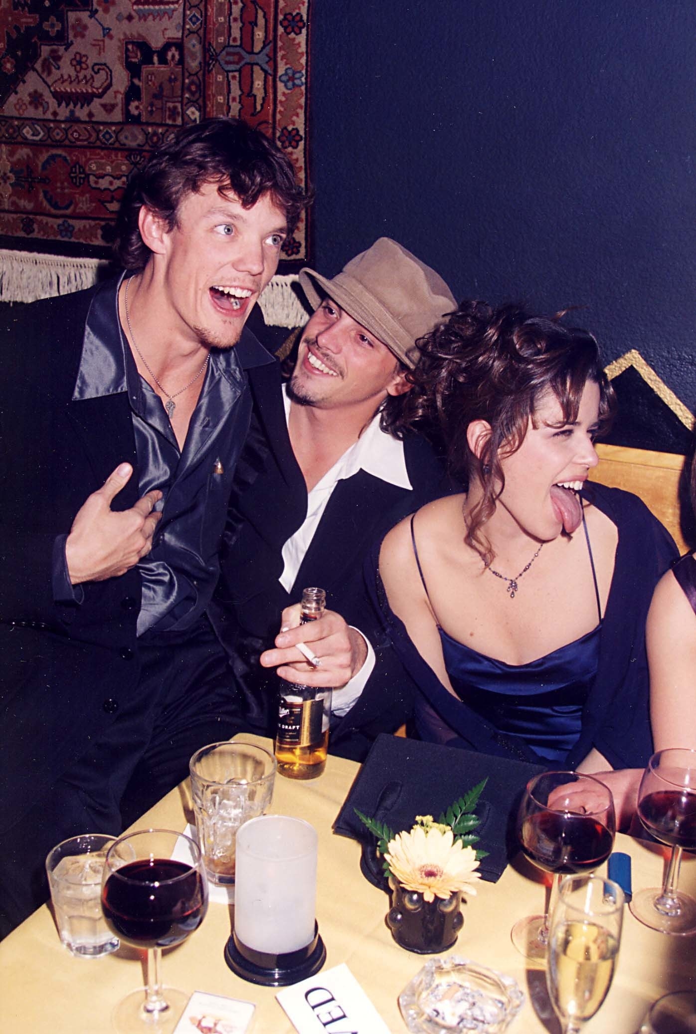 Matthew Lillard, Skeet Ulrich, and Neve Campbell happily sitting at a table with glasses of wine