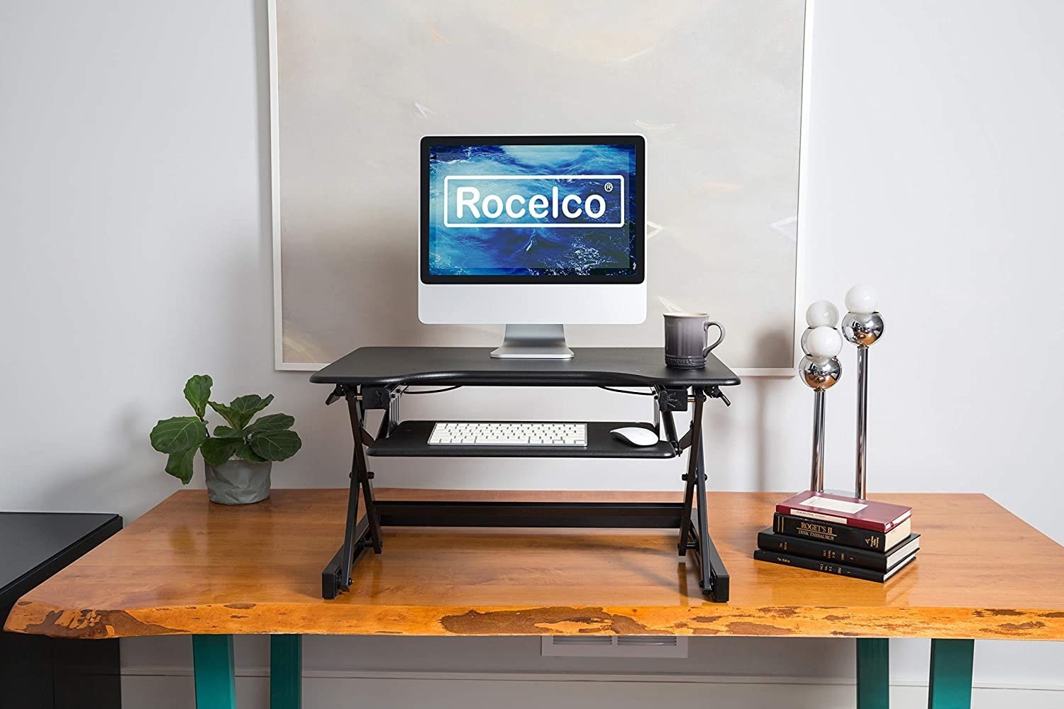 The monitor riser on a larger wooden desk with a monitor, keyboard, and mug on top of it