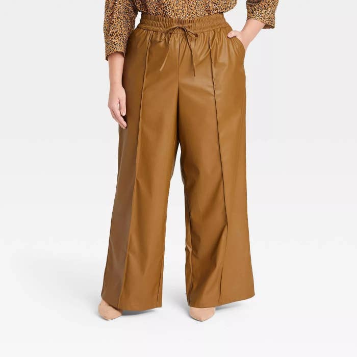 Model wearing camel colored pants with thick line detailing on each leg