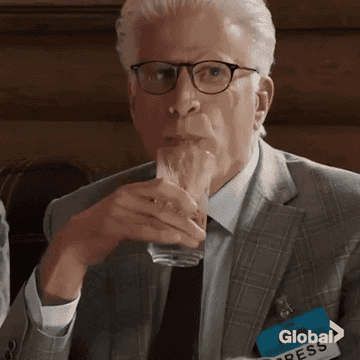 Ted Danson as Michael takes a sip of a drink before immediately spitting it back into the glass before covering his mouth with his hand and wincing in &quot;The Good Place&quot;