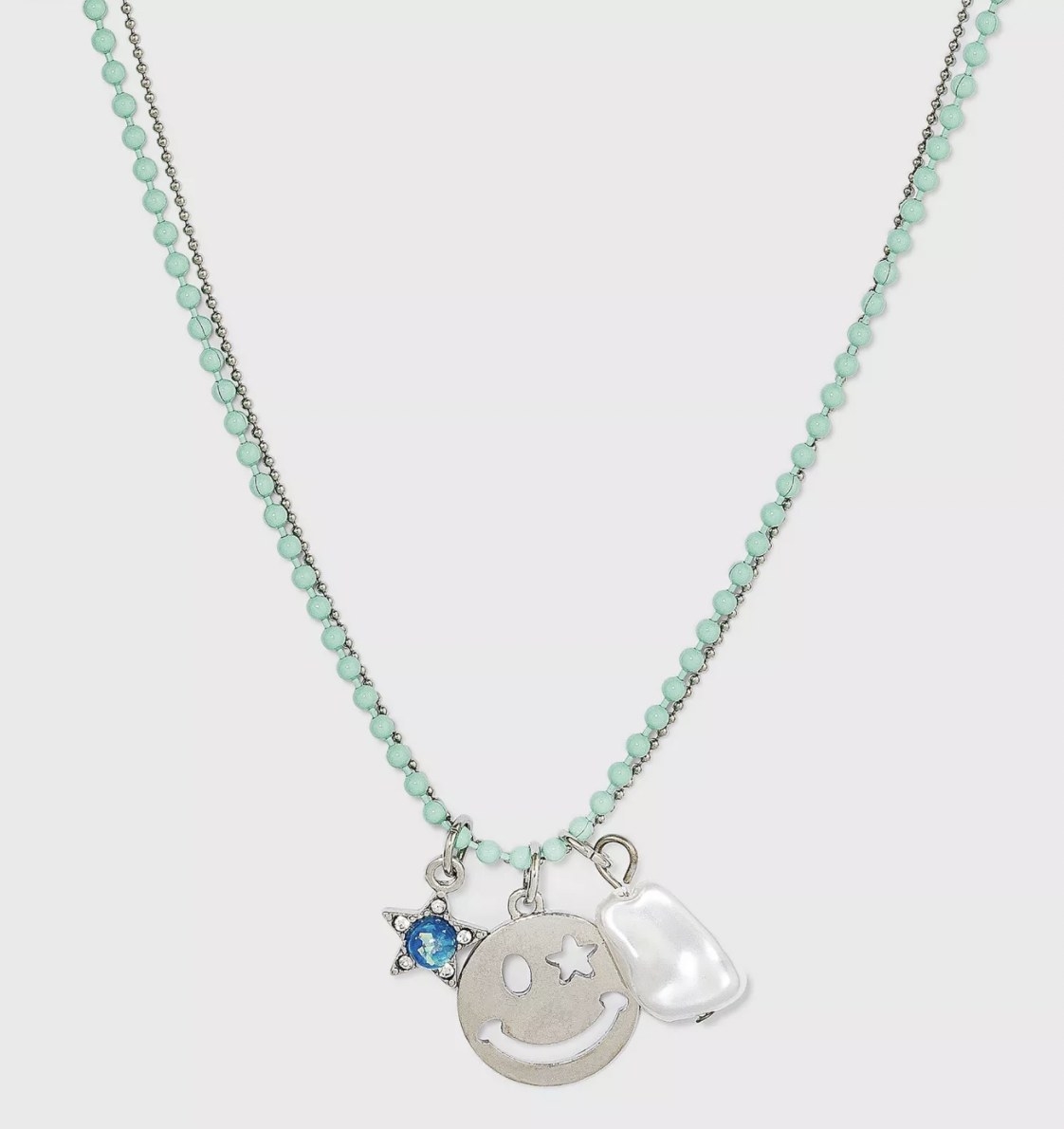 a necklace with a turquoise chain and silver chain with a blue and silver star, silver smiley face, and a freshwater pearl charm