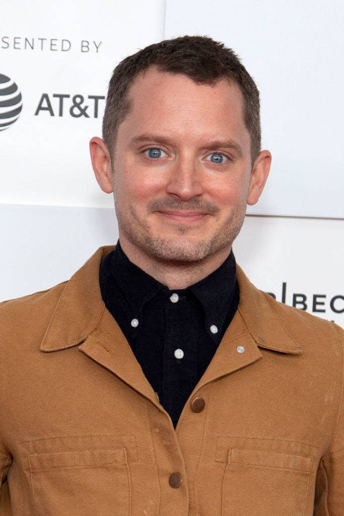 Elijah Wood smiling on the red carpet with short hair and a button up shirt and casual jacket