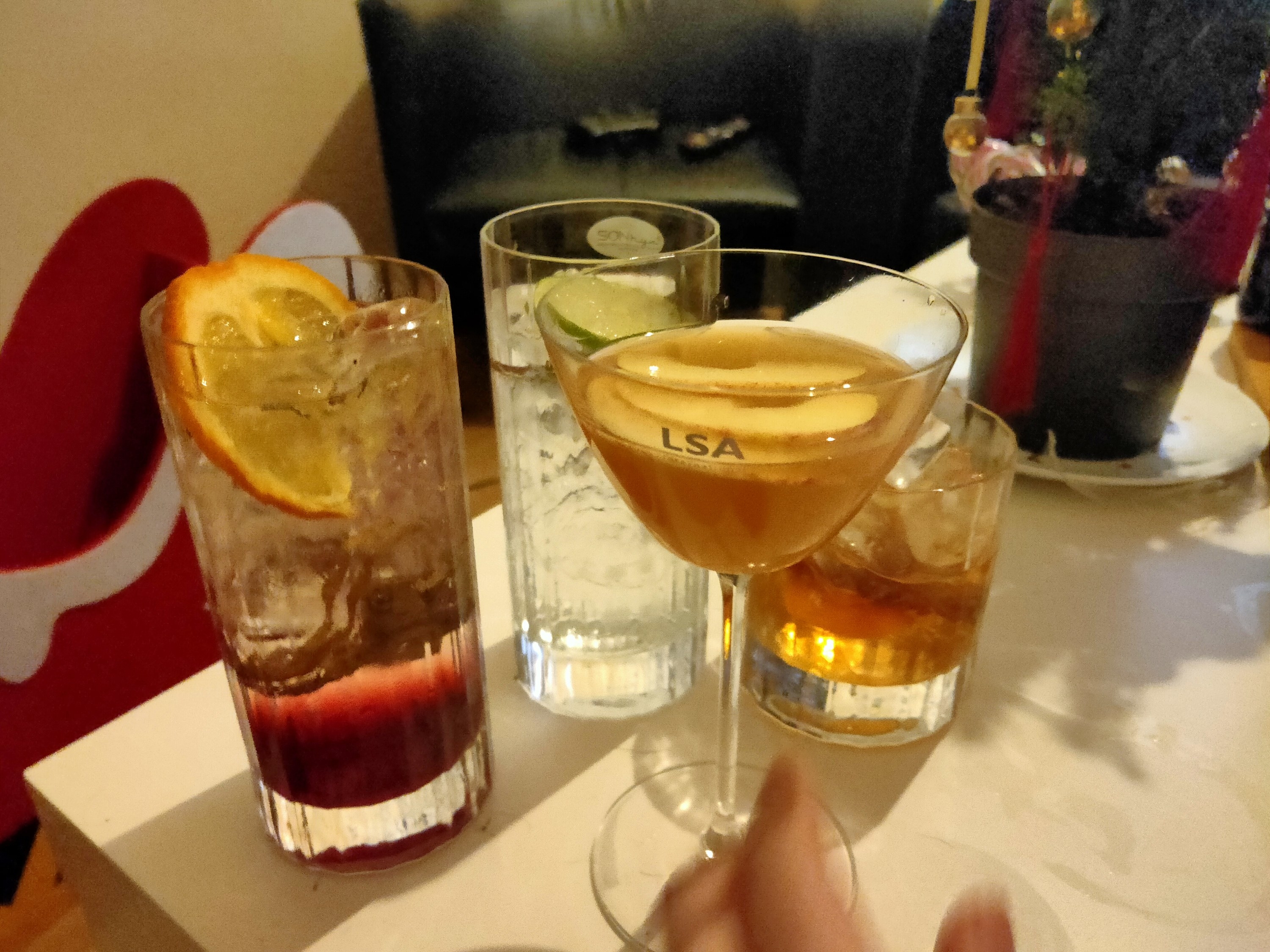 the four completed cocktails sitting on a table top with a hand reaching out to grab the lynd martini