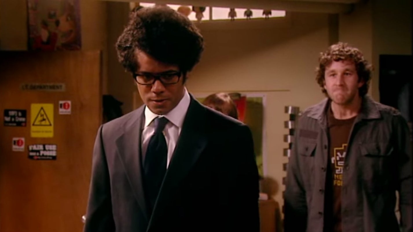 Moss standing in a suit and tie with his back turned to Roy and Jen in &quot;The IT Crowd&quot;