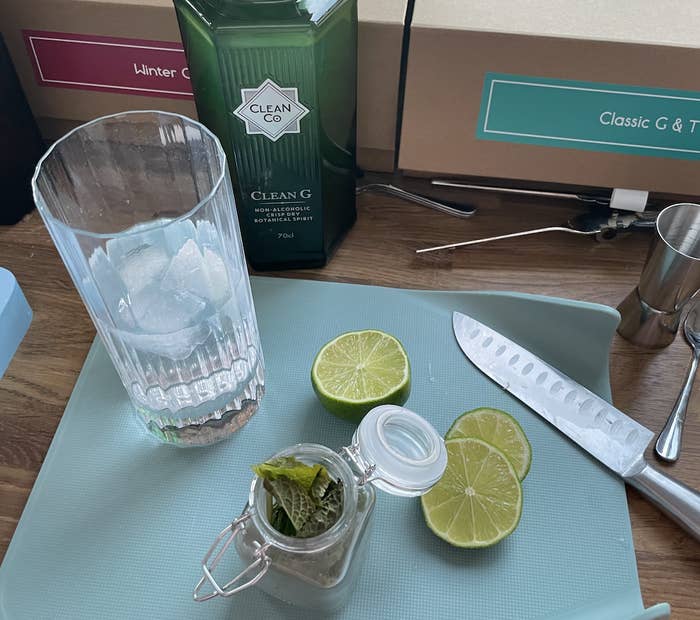 a bottle of clean g next to ingredients for a gin and tonic including a sliced lime some mint and a glass full of ice and tonic water