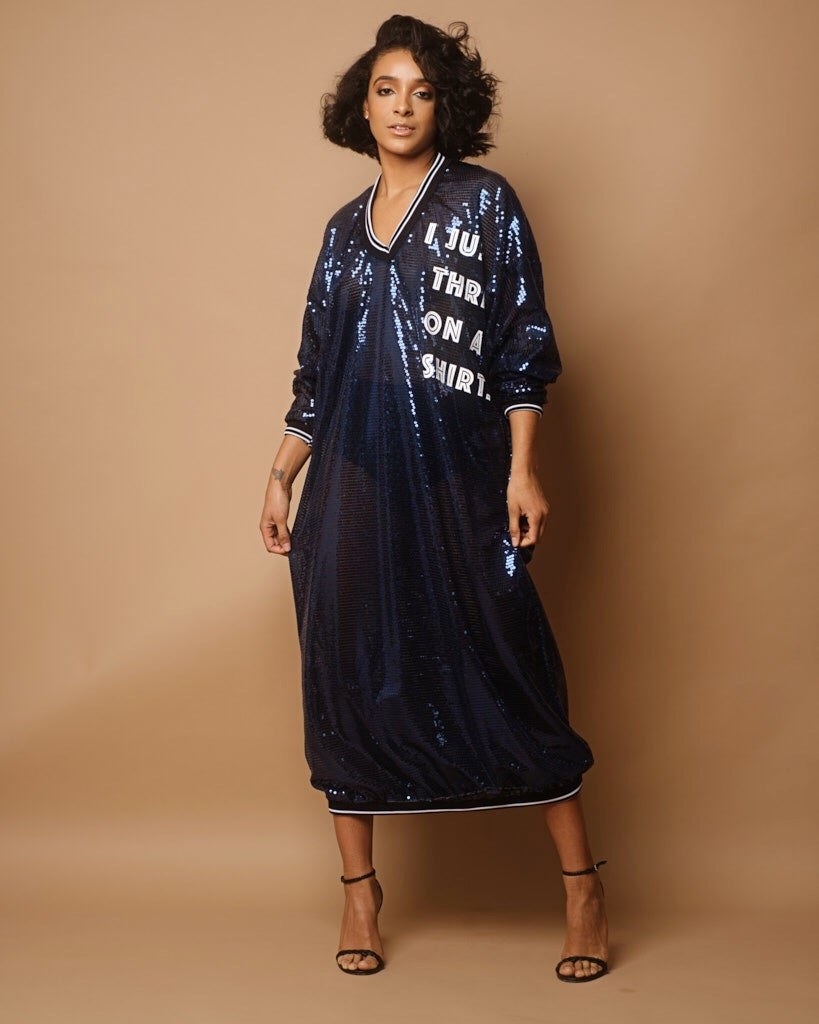 model in calf-length, long-sleeve v neck sheer navy sequin dress with black trim and white wording