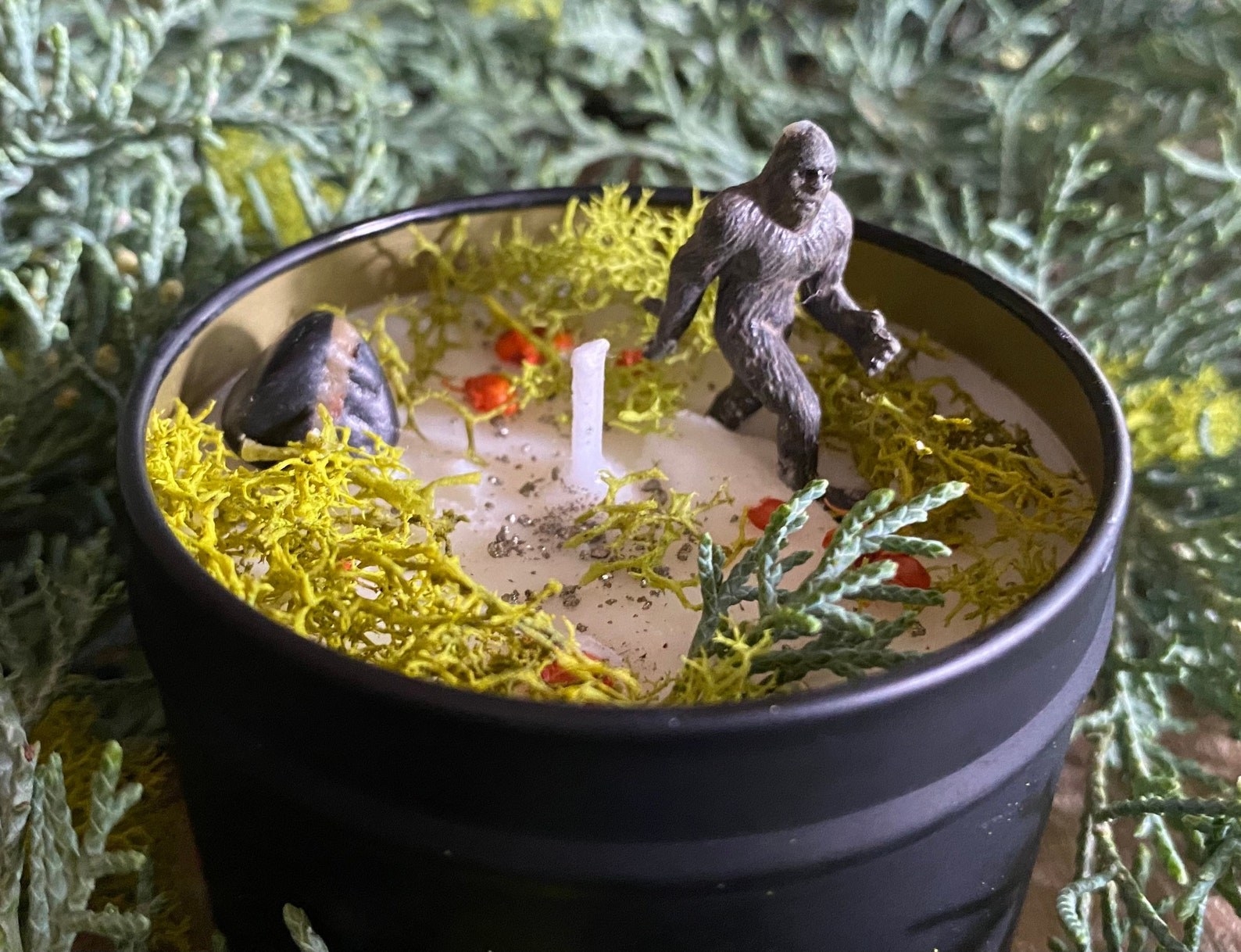 The Sasquatch candle surrounded by greenery