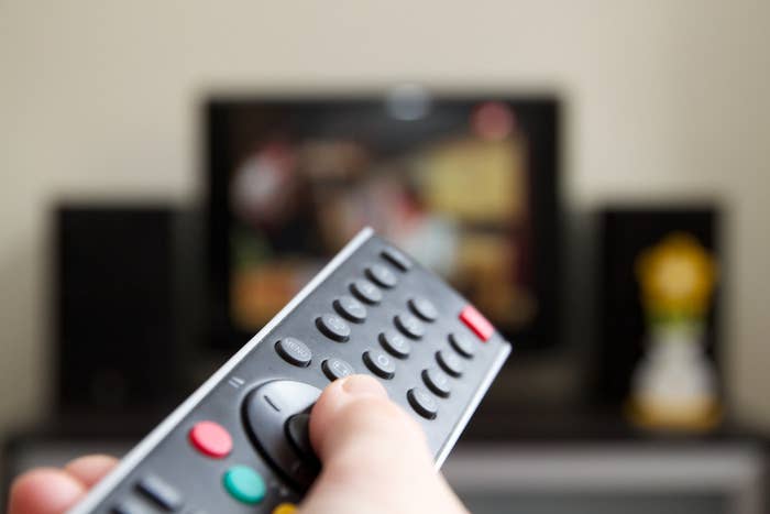 Hand holding remote control changing Channels with television set.