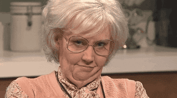 Kate McKinnon dressed as an old person and winking at the camera on