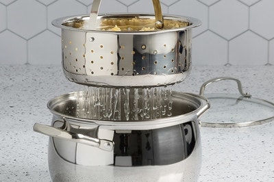 There is large stainless steal pot underneath a smaller one with holes draining pasta