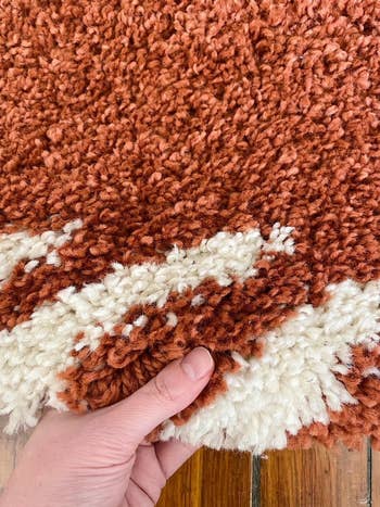 close up of buzzfeeder's hand holding up the rug to show how plush it is