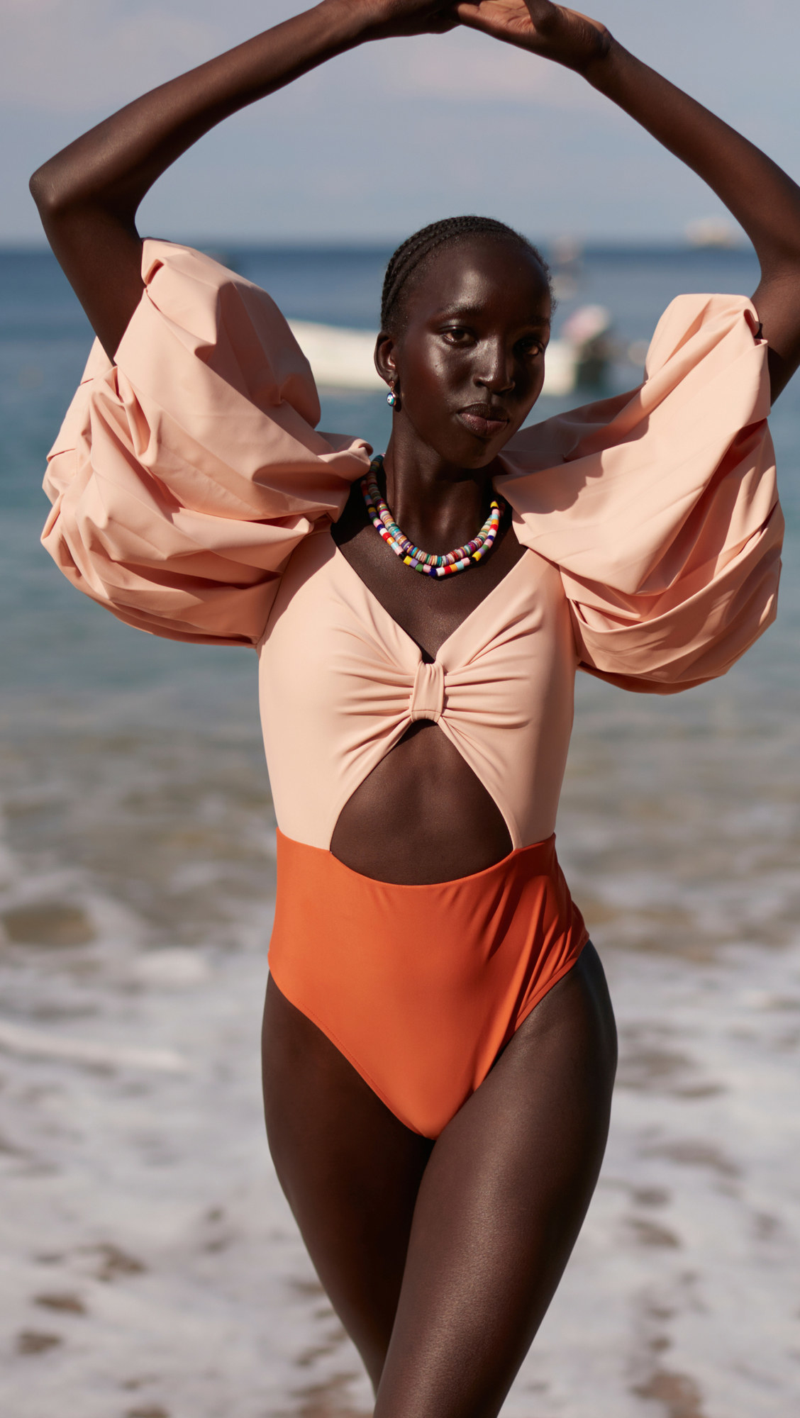 model in the color-blocked pale pink and orange one-piece with waist cutout and super voluminous sleeves