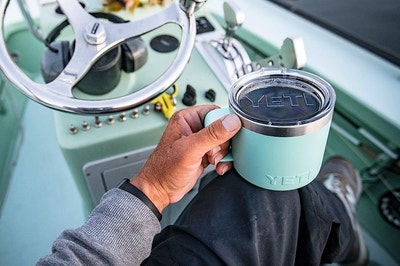 a model holding a mint green yeti mug while sitting on a boat