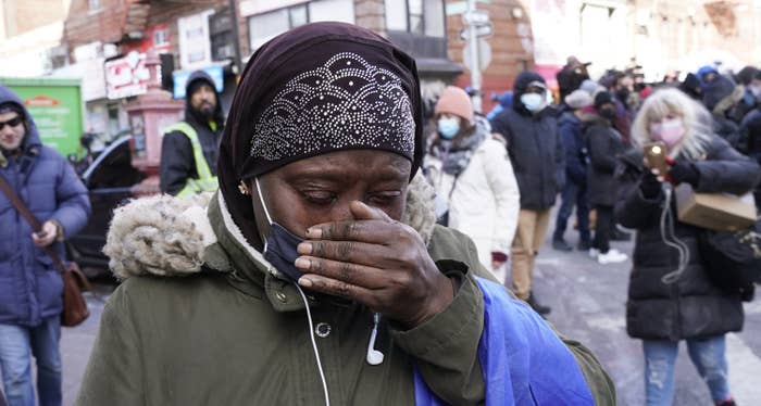 A woman on the street wears a thick winter jacket and face mask and covers her mouth and nose with one hand