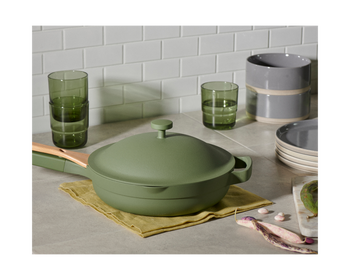 the green always pan on a kitchen counter surrounded by cups, bowls, and plates