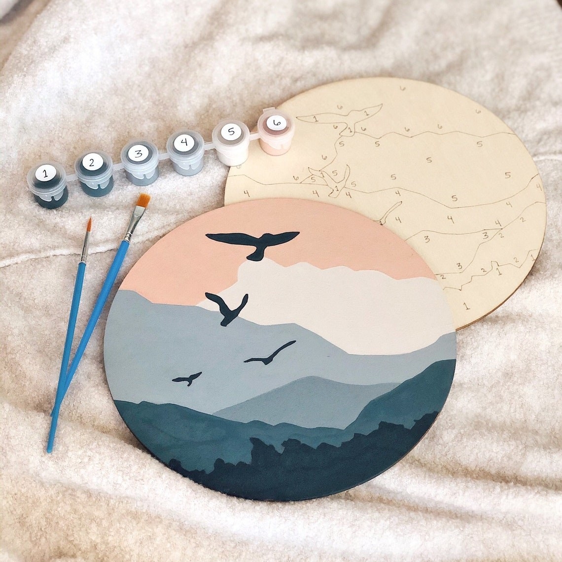 a round wooden plaque with a design outlined on it and paints to use