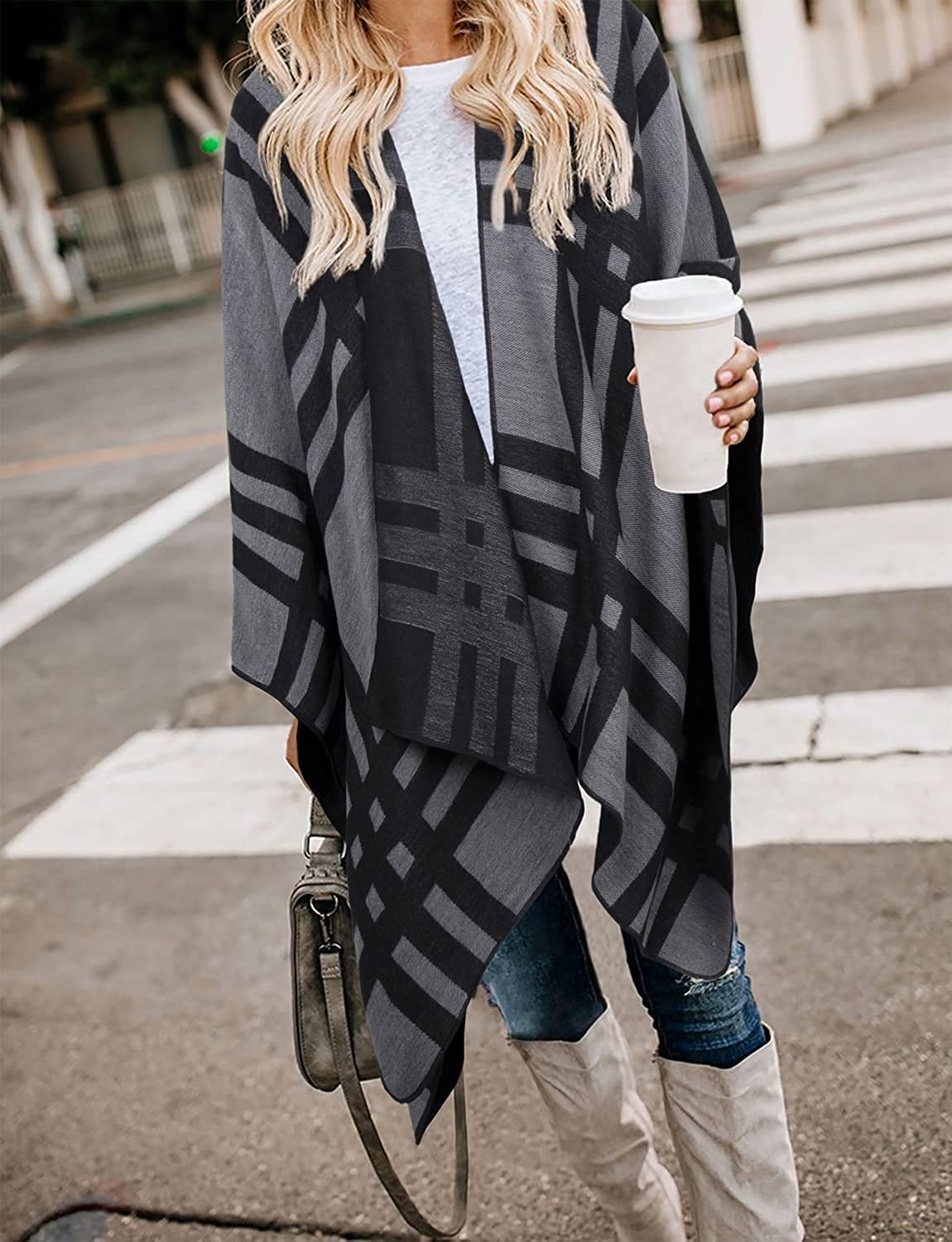 A person standing on the street wearing the oversized blanket shawl carrying coffee and a purse