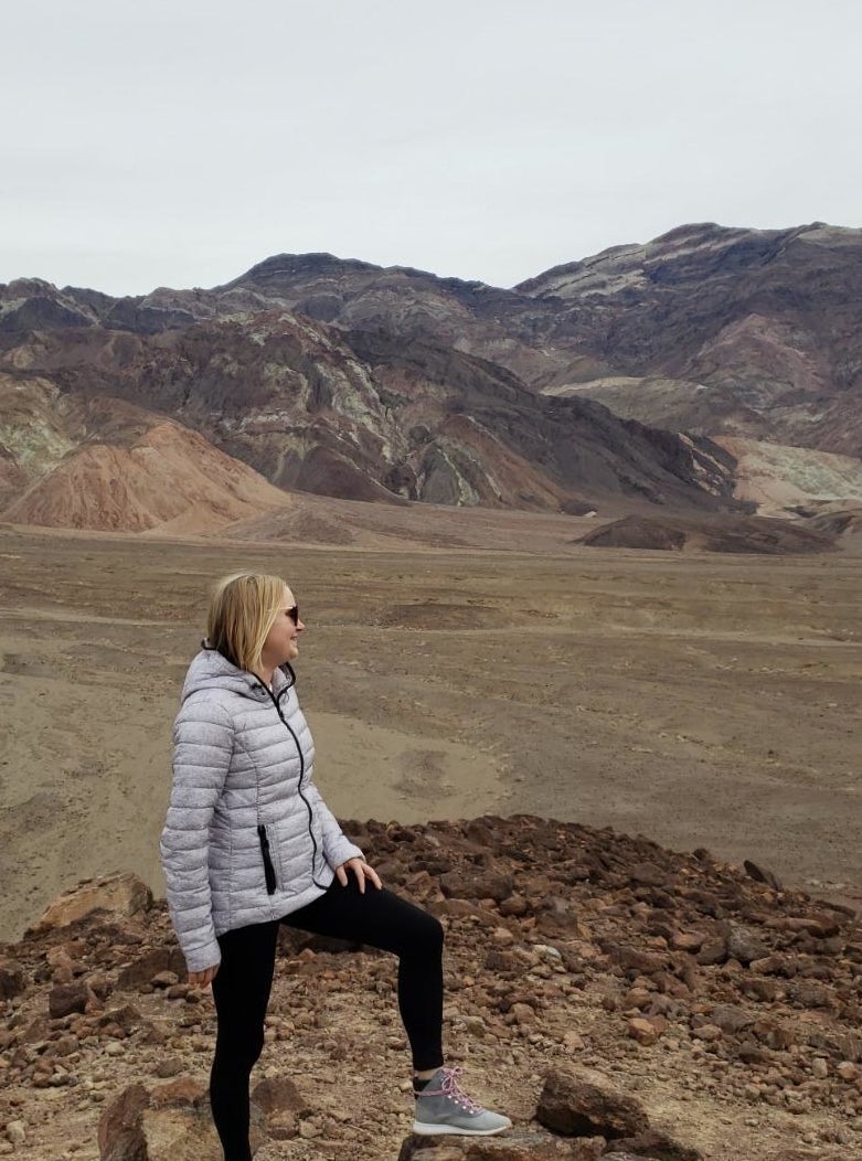 Reviewer wearing white quilted puffer jacket with sneakers in front of mountain landscape