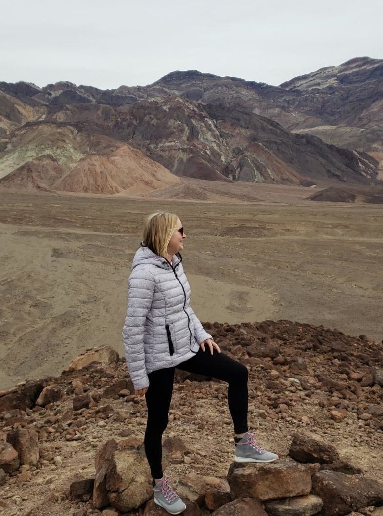 Reviewer wearing white quilted puffer jacket with sneakers in front of mountain landscape