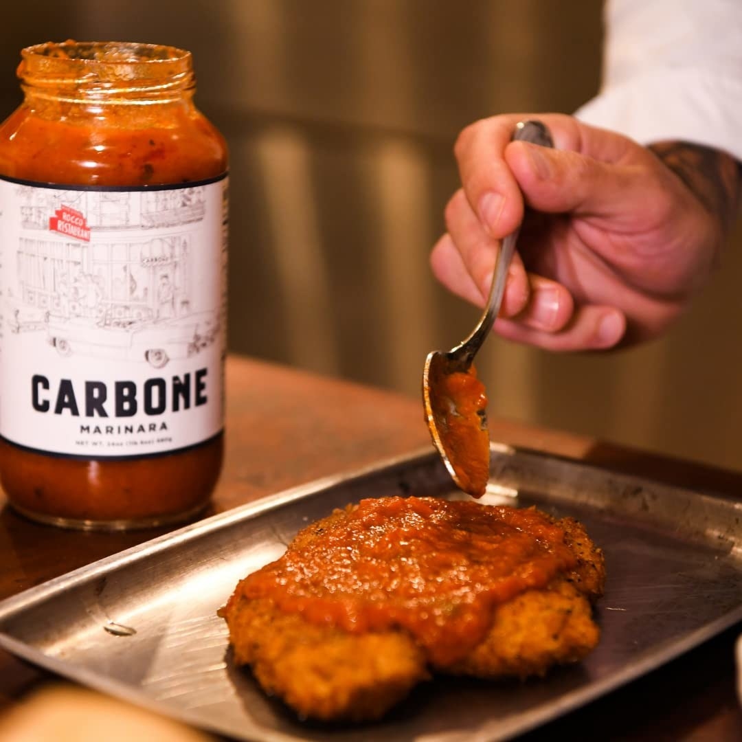 person putting sauce on a piece of chicken for chicken parm