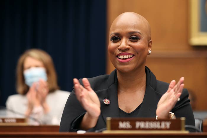 Rep. Ayanna Pressley smiles while sitting in a congressional meeting