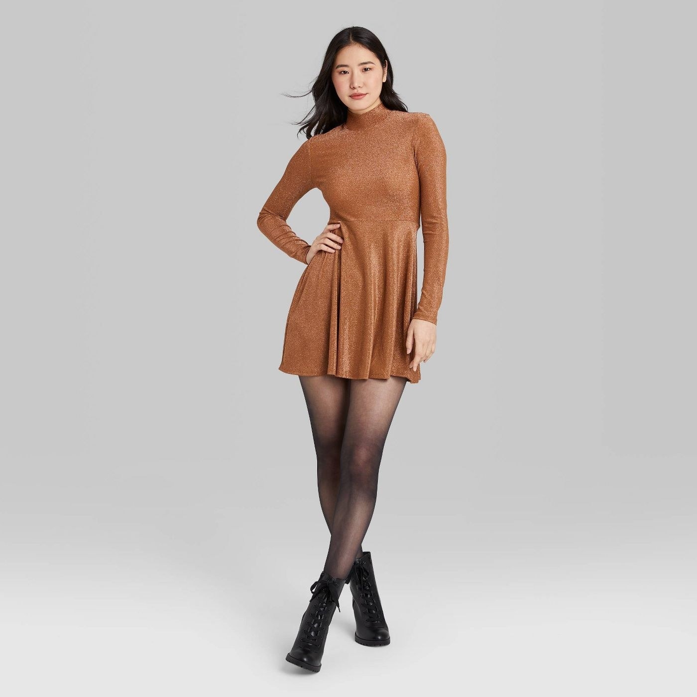 a model wearing the copper sparkly dress with black tights and black boots