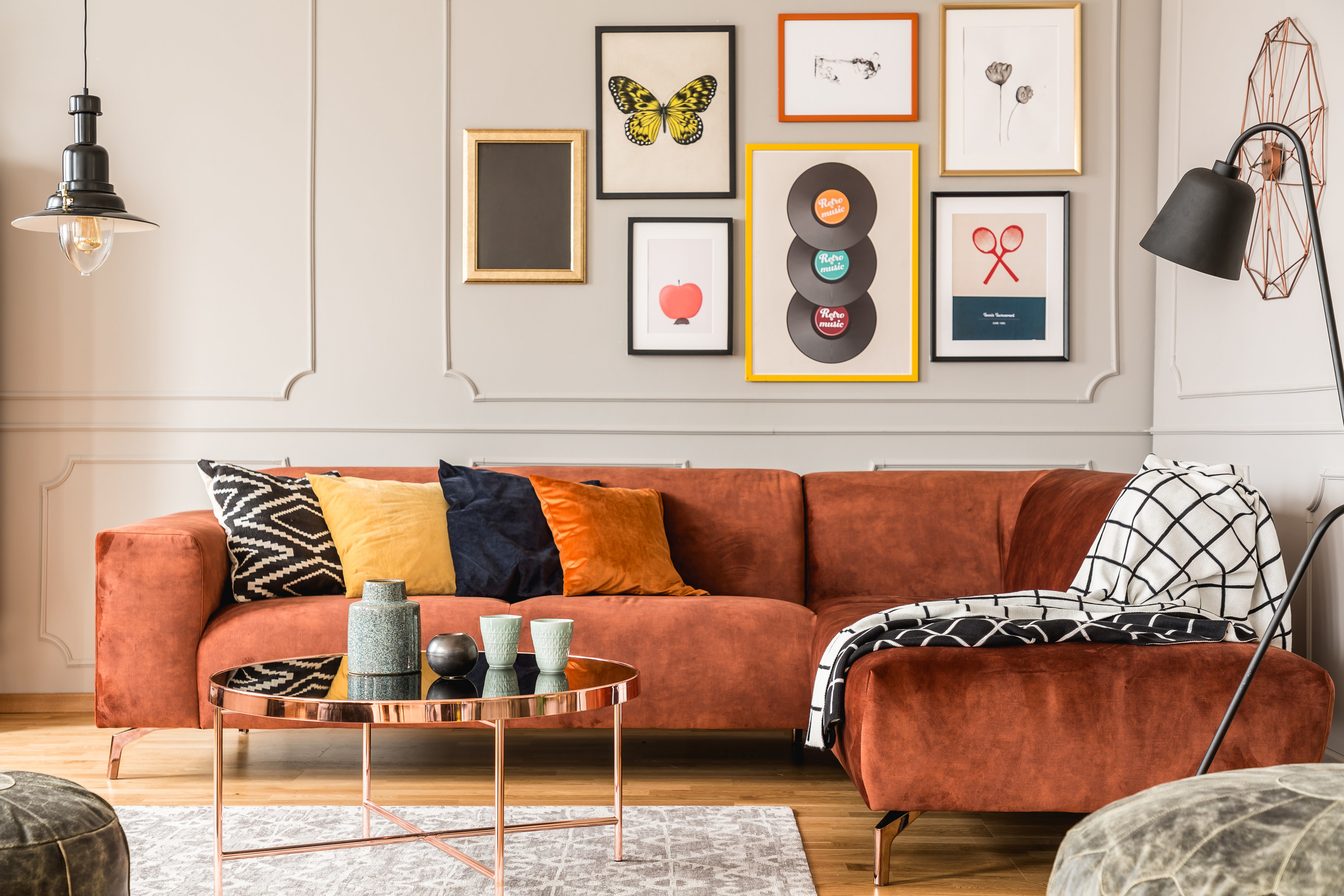A living room with a bright orange sofa, the wall behind it is covered in photo frames