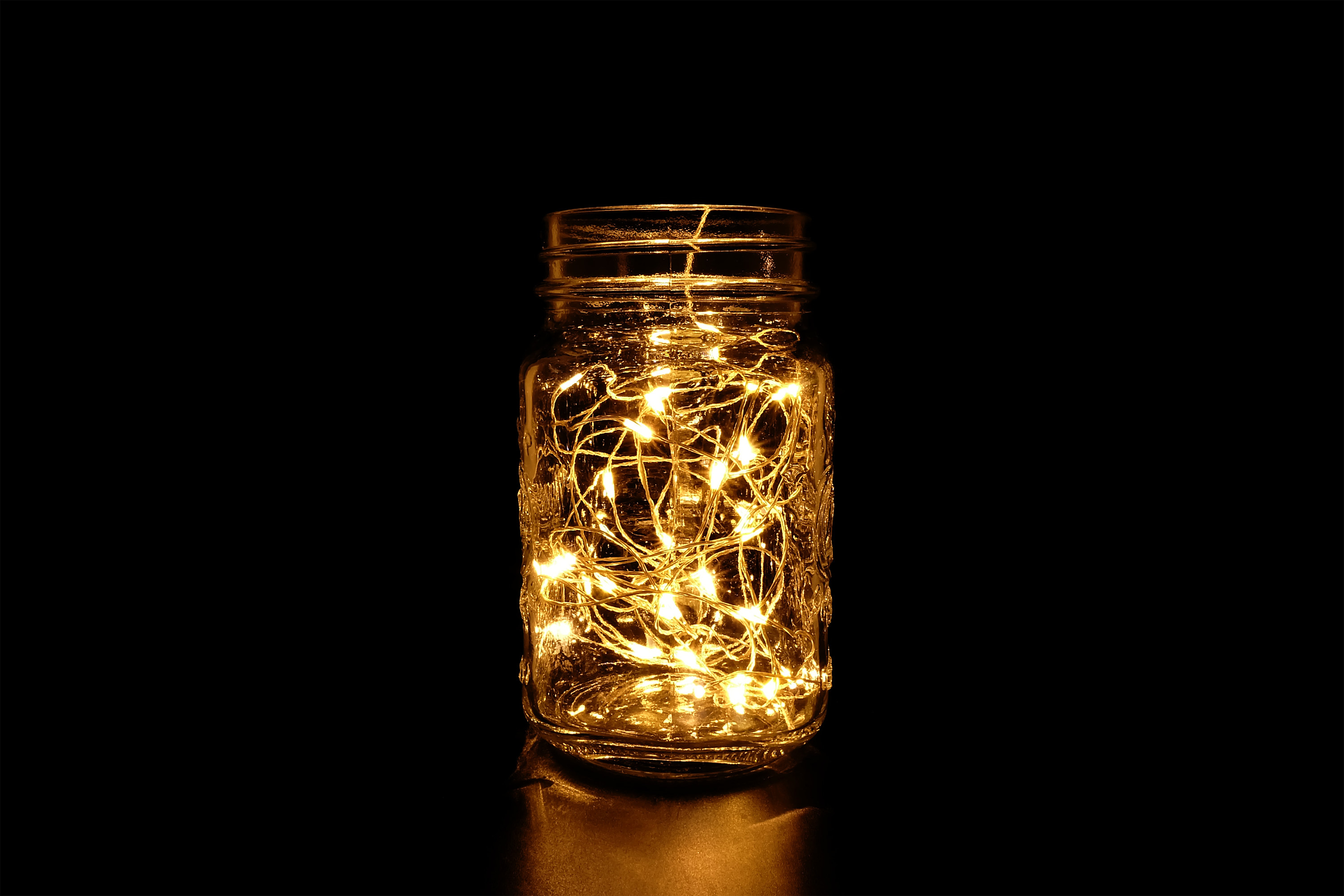 A strand of lit fairy lights inside a glass Mason jar