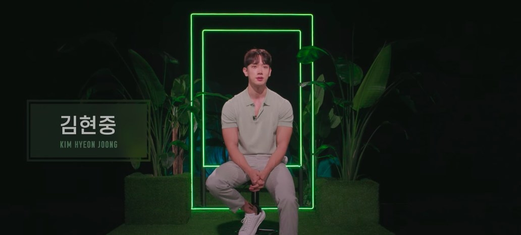 Kim Hyeon-joong sits on a stool in a green and black room.