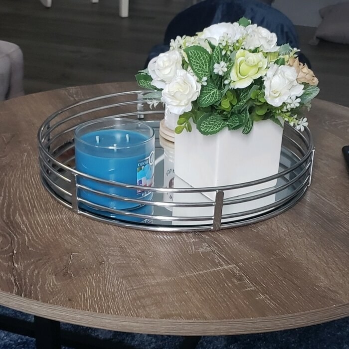 A reviewer&#x27;s photo of the silver tray holding a candle, coasters, and vase of flowers on their coffee table