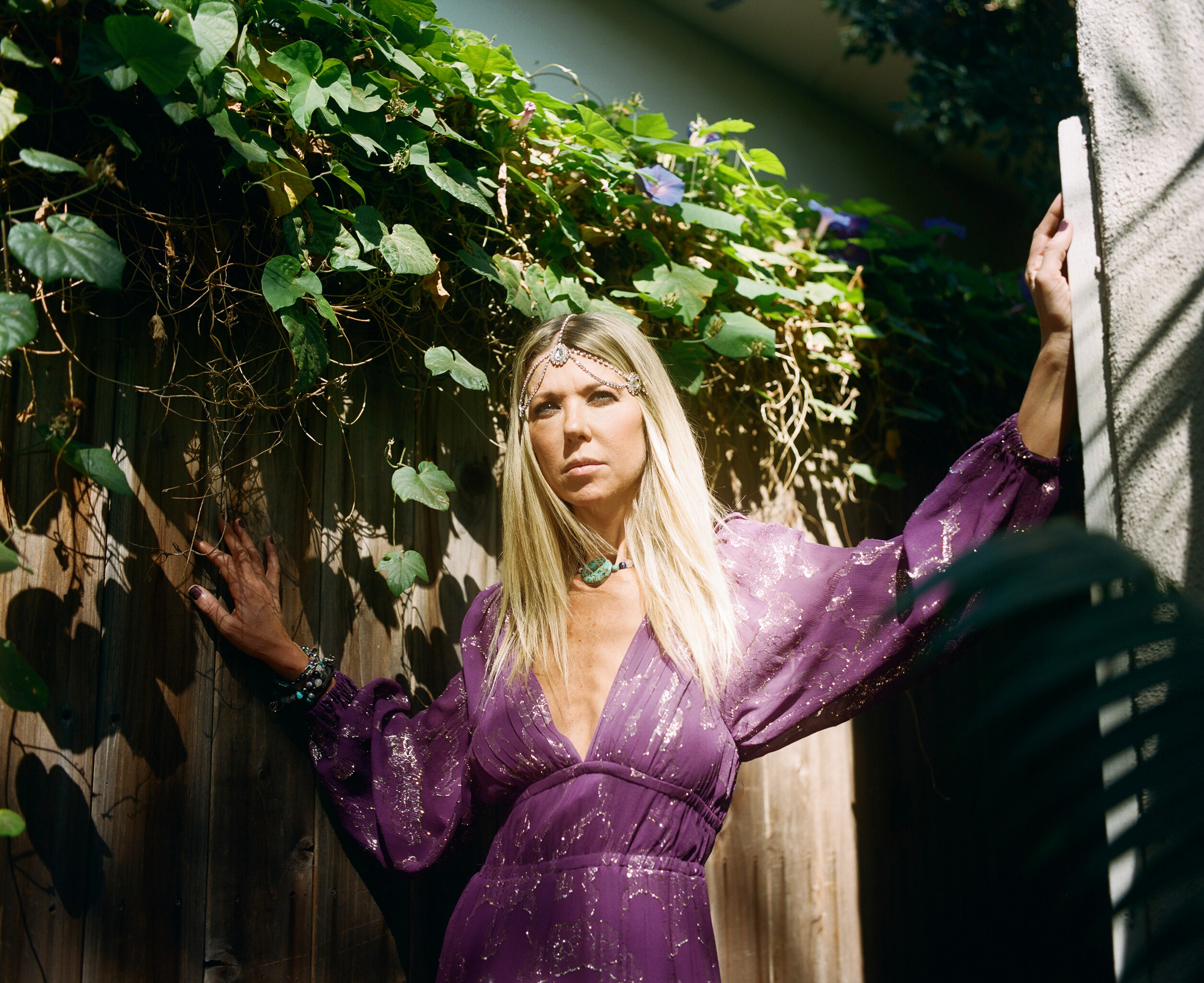 Tara Reid in a purple dress in front of a fence covered in vines 