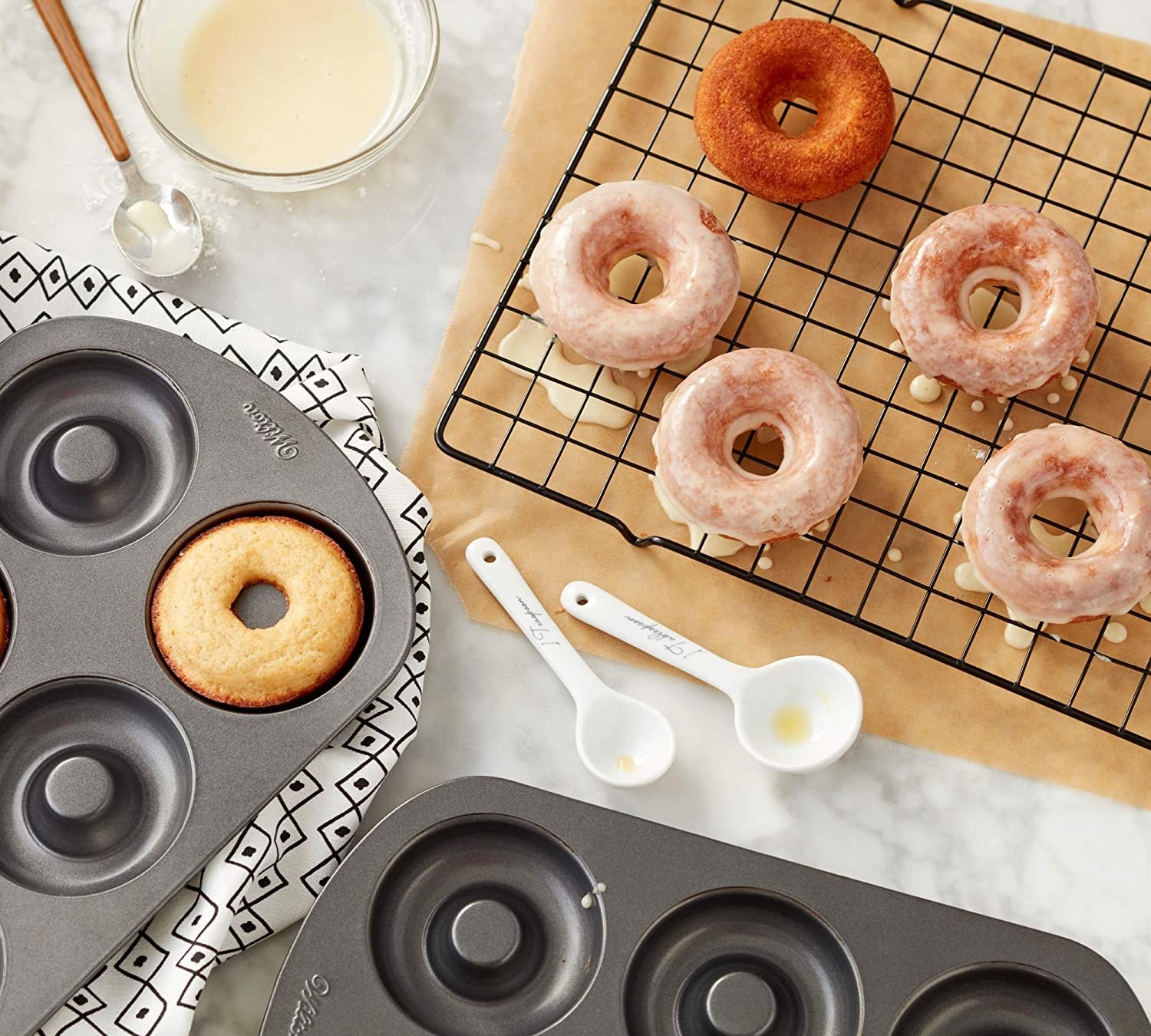 Two donut pans and a donuts on a cooling rack on a counter