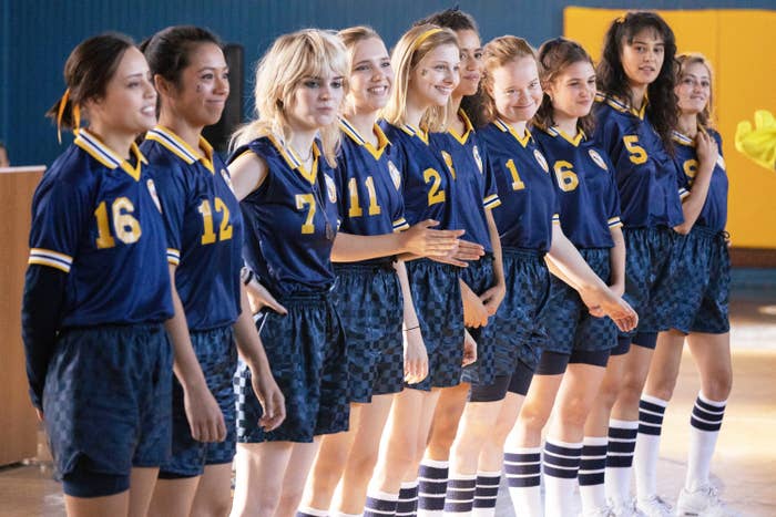 A group of girls in soccer uniforms lined up inside of a gym