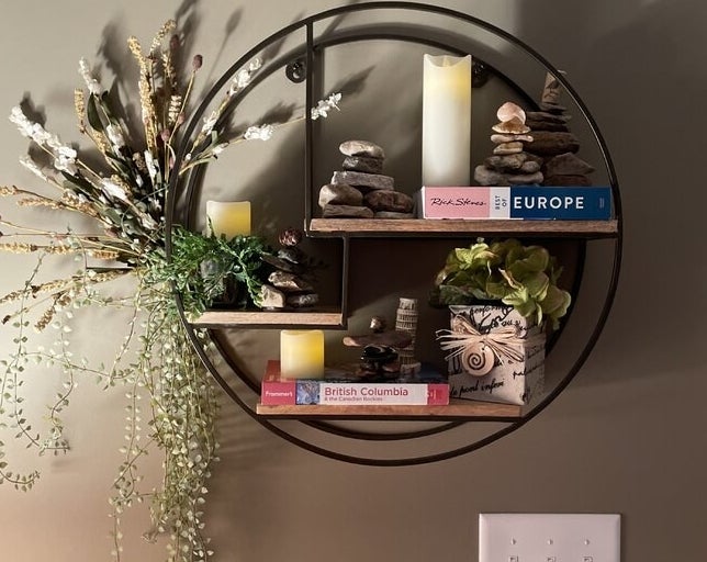 A reviewer&#x27;s photo of the shelf displaying rocks, books, candles, and greenery