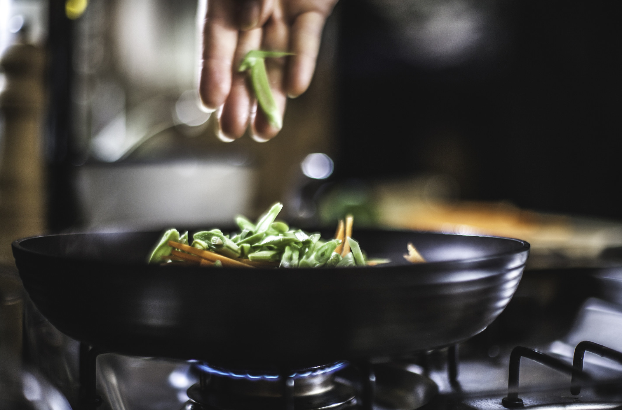 Putting vegetables in a pan on the stove.