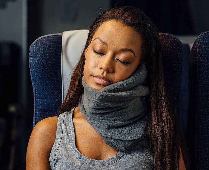 Model wearing a gray Trtl pillow while sleeping on a plane