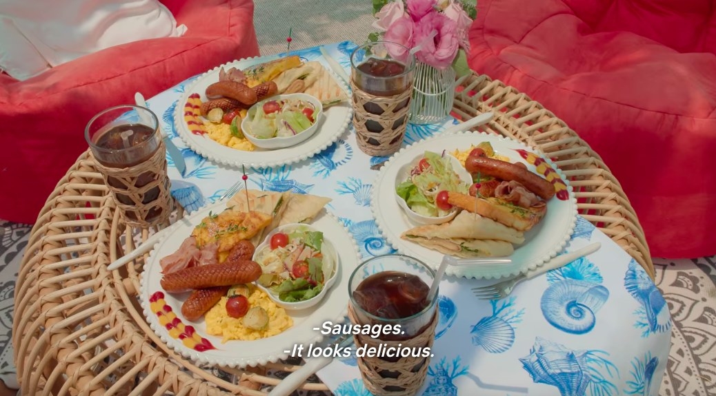 Thee plates of food and three iced Americans sit on a rattan table decorated with flowers