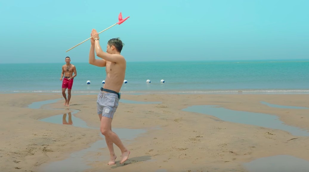 Se-hoon claps while holding a flag on the beach, Jin-taek lags behind